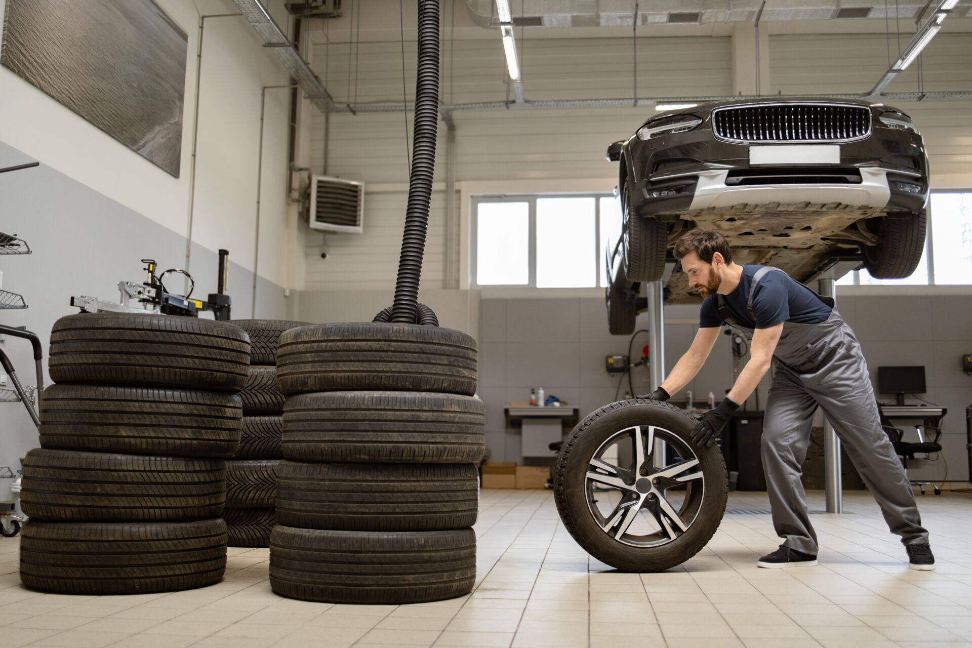 Ein Mechaniker rollt einen Reifen in einer Werkstatt unter einem aufgebockten Auto. Reifendienst Böhme in Vetschau bietet professionelle Reifenmontage.