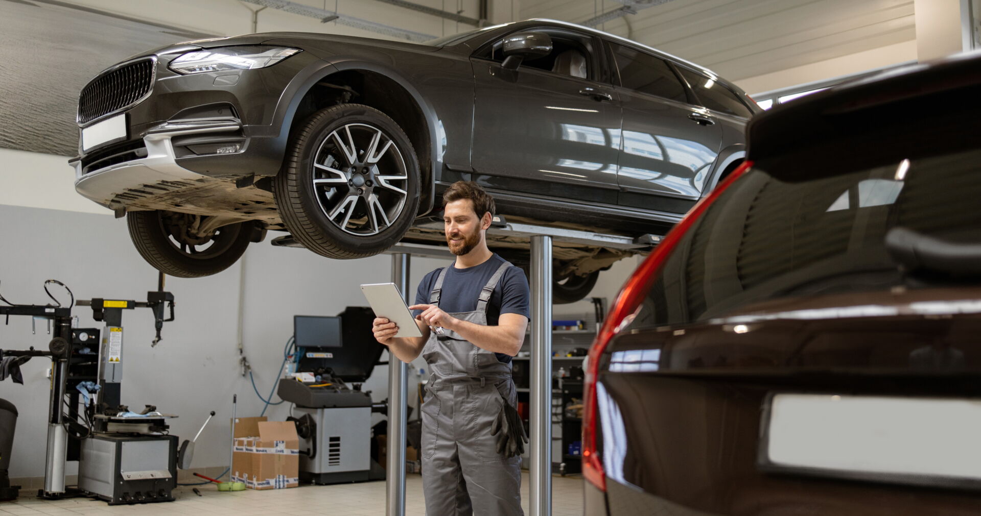 Ein Mechaniker mit Tablet unter einem aufgebockten grauen SUV in einer Werkstatt. Reifendienst Böhme in Vetschau bietet moderne Fahrzeugdiagnose.