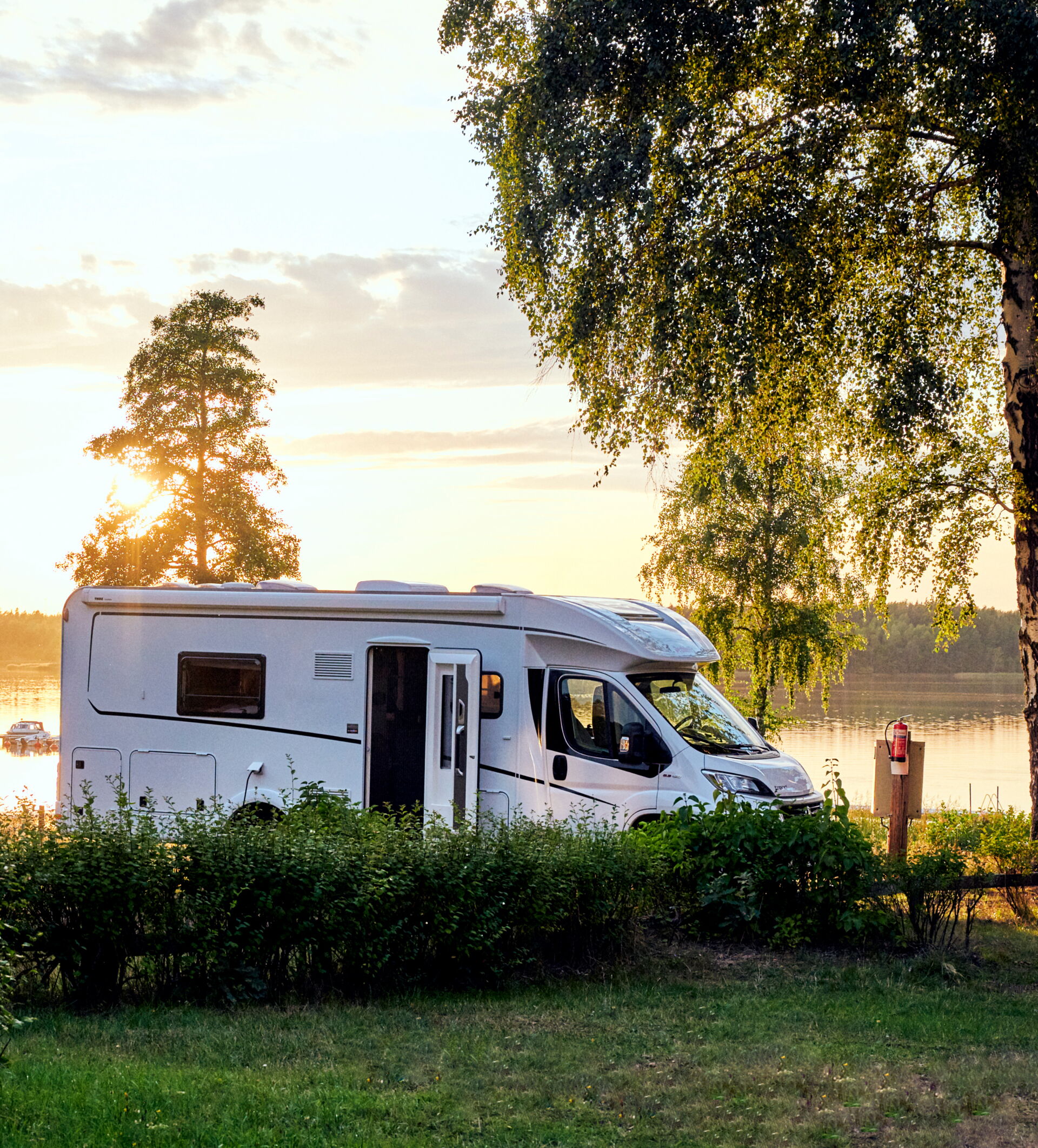 Ein weißes Wohnmobil steht am Ufer eines Sees bei Sonnenuntergang. Vermietung durch Reifendienst Böhme in Vetschau.